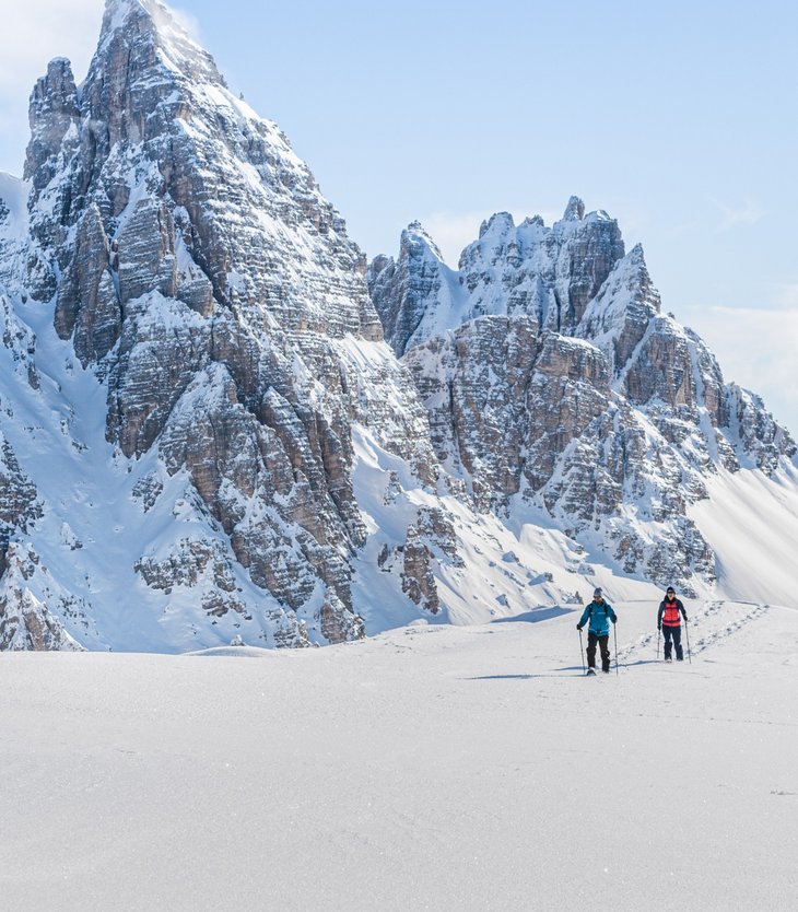 Zwei Skitourengeher fahren vor verschneitem Bergpanorama im Sonnenschein