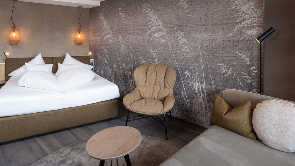 Modern hotel room with double bed, armchair, and sofa against a wall with reed pattern