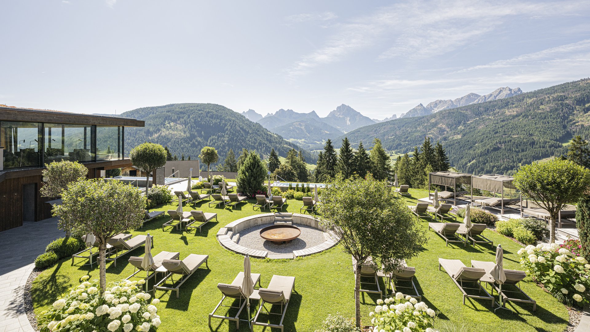 Hotelgarten mit Liegestühlen, Feuerstelle und Blick auf die Berge