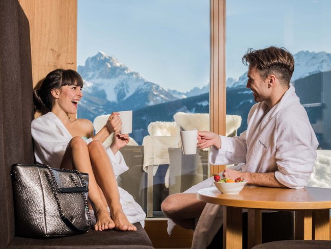 Alpen Tesitin: il vostro hotel con spa tra le Dolomiti Coppia in accappatoi beve caffè con vista sulle montagne in stanza soleggiata