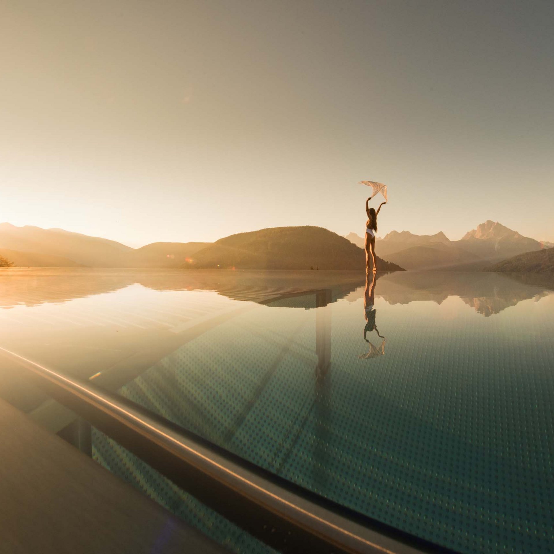 Woman on edge of infinity pool with sunset and mountain view