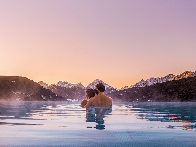 Paar entspannt im beheizten Pool mit Bergblick bei Sonnenuntergang