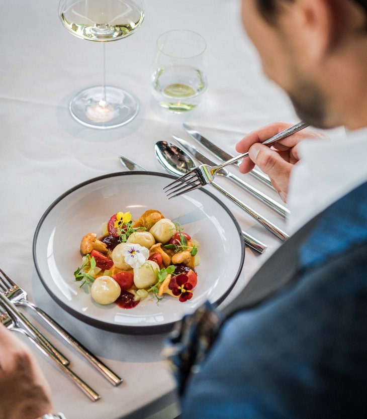 Your 5-star hotel in Val Pusteria/Pustertal: Alpen Tesitin Man eating fine dish with mushrooms, tomatoes and edible flowers in upscale restaurant