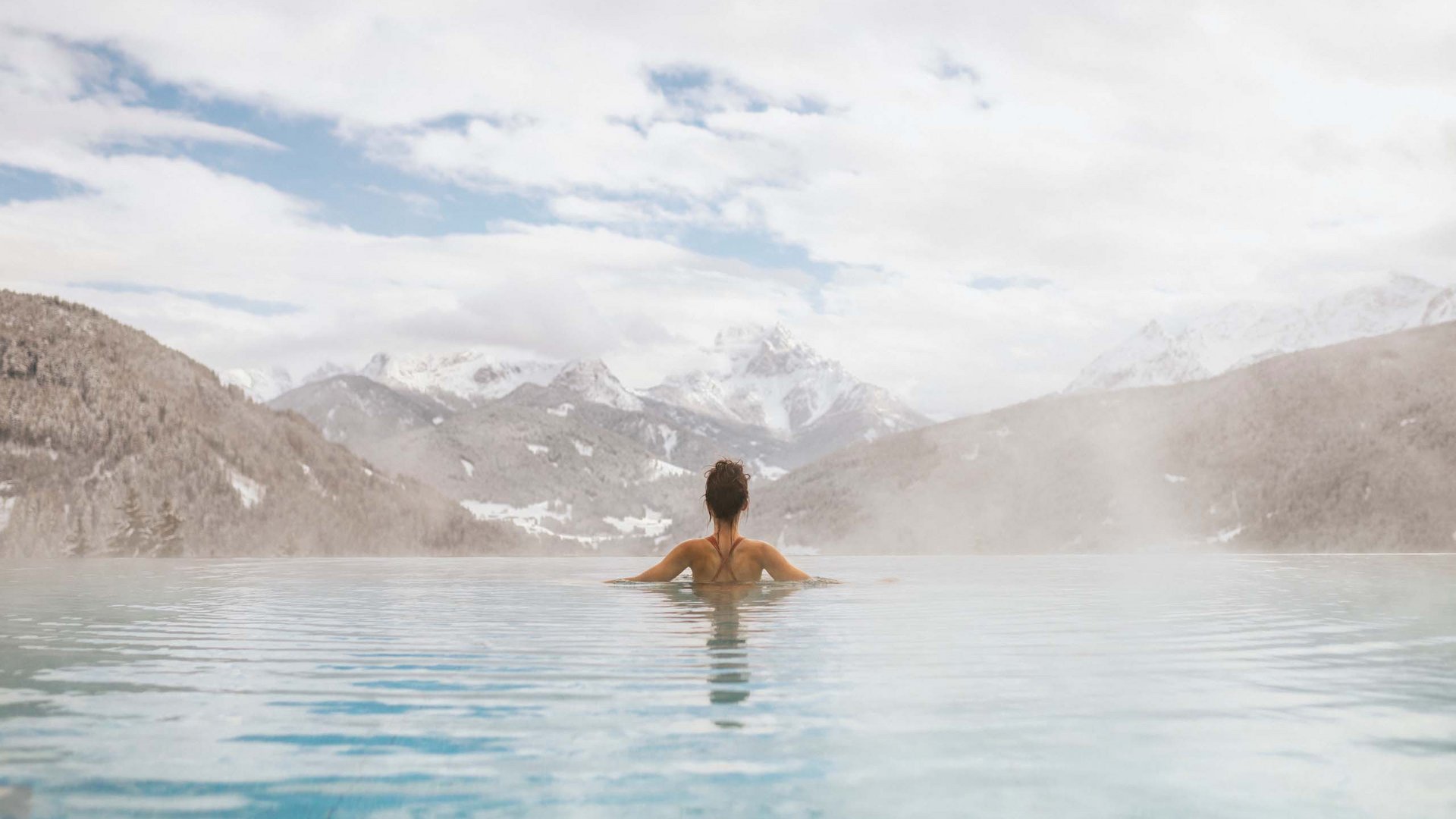 Donna rilassata in piscina all'aperto con vista sulle montagne e nebbia