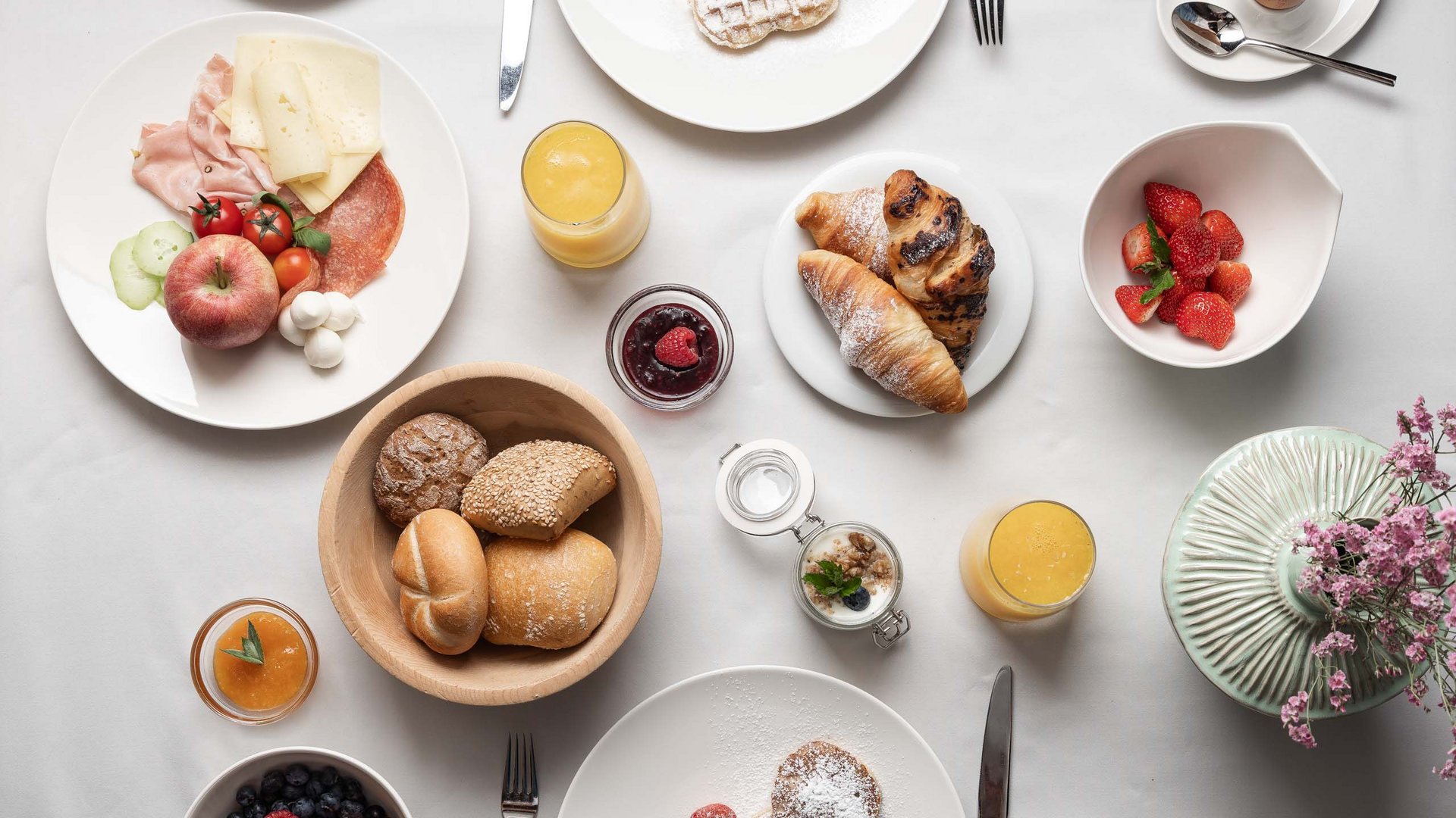 Verschiedene Frühstücksgerichte auf weißem Tisch mit Kaffee, Obst und Gebäck