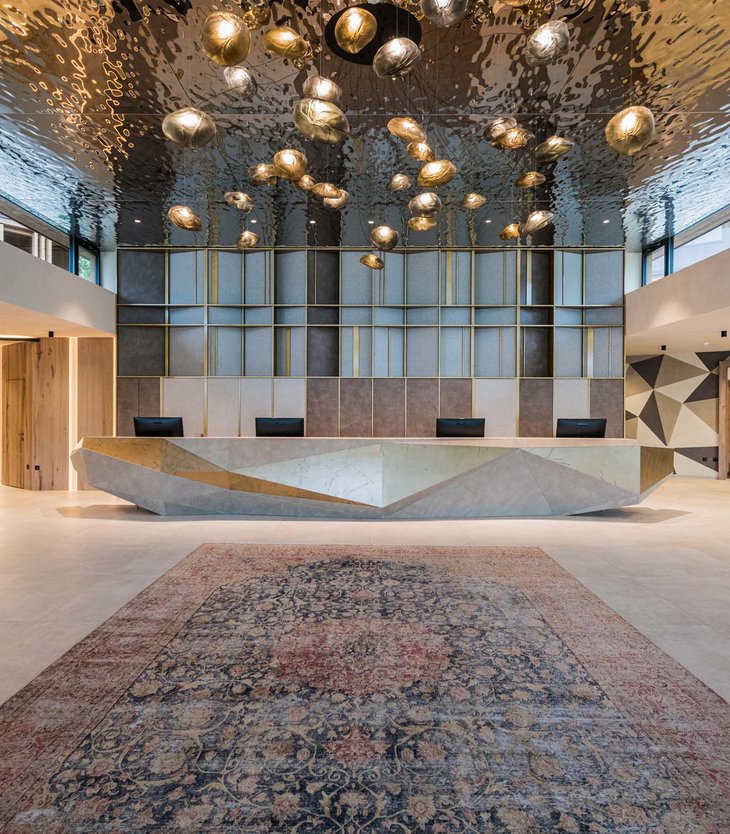 Your 5-star hotel in Val Pusteria/Pustertal: Alpen Tesitin Modern lobby with geometric reception desk and sculptural ceiling lights