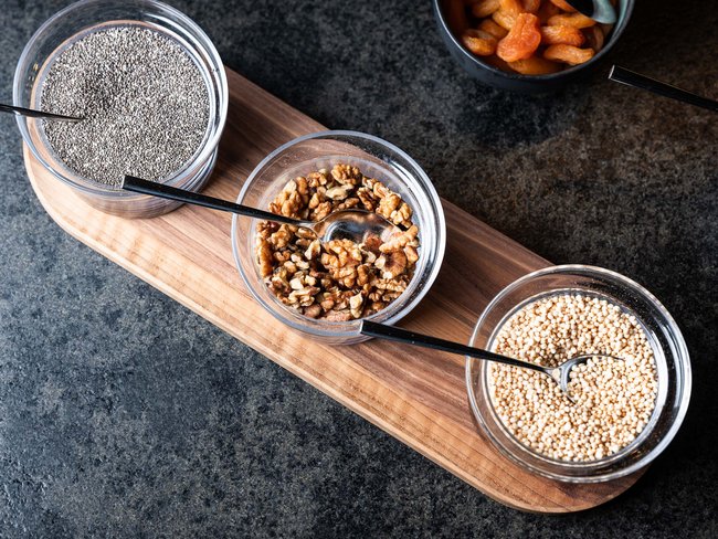 Ciotole con semi di chia, noci e quinoa su un tagliere di legno