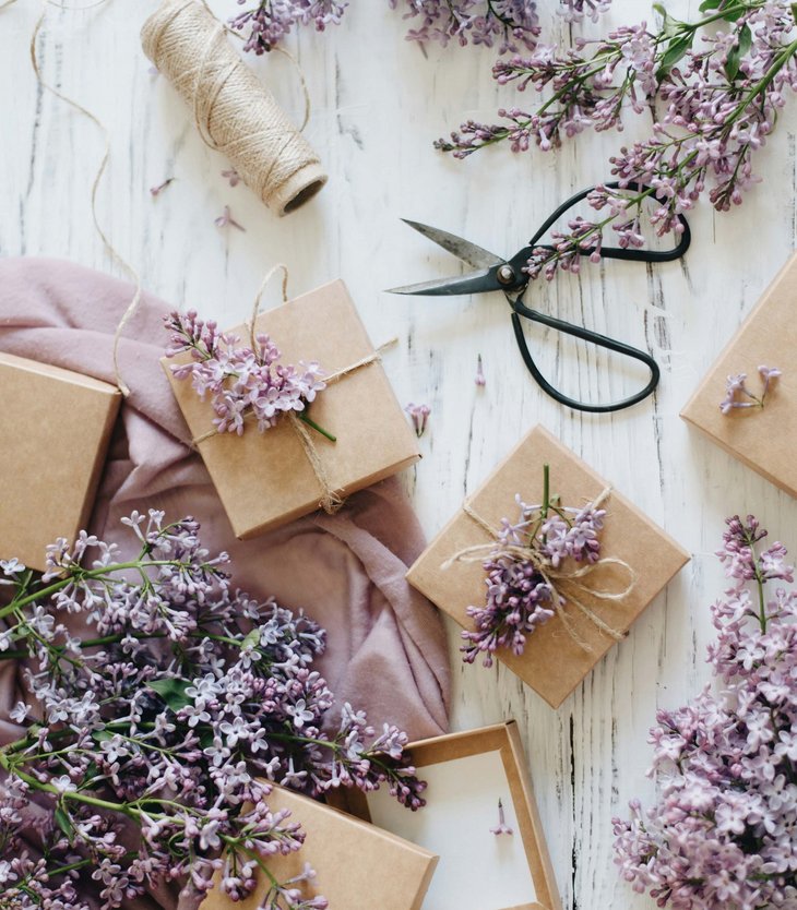 Geschenkverpackung mit lila Fliederblüten und Bast auf weißem Holztisch