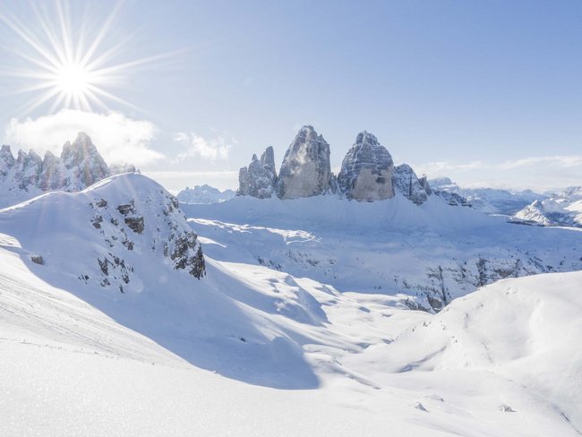 Paesaggio invernale soleggiato con montagne innevate e cielo blu chiaro