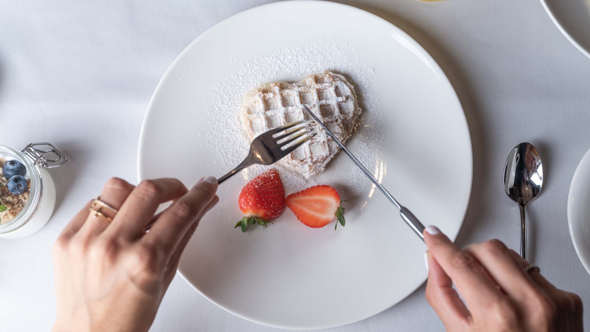 Waffle a forma di cuore con zucchero a velo e fragole su piatto bianco