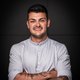 Young chef with crossed arms and tattoos against a dark background