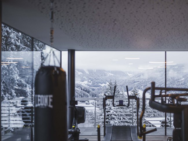Fitnessraum mit Boxsack und Laufband vor verschneiter Berglandschaft