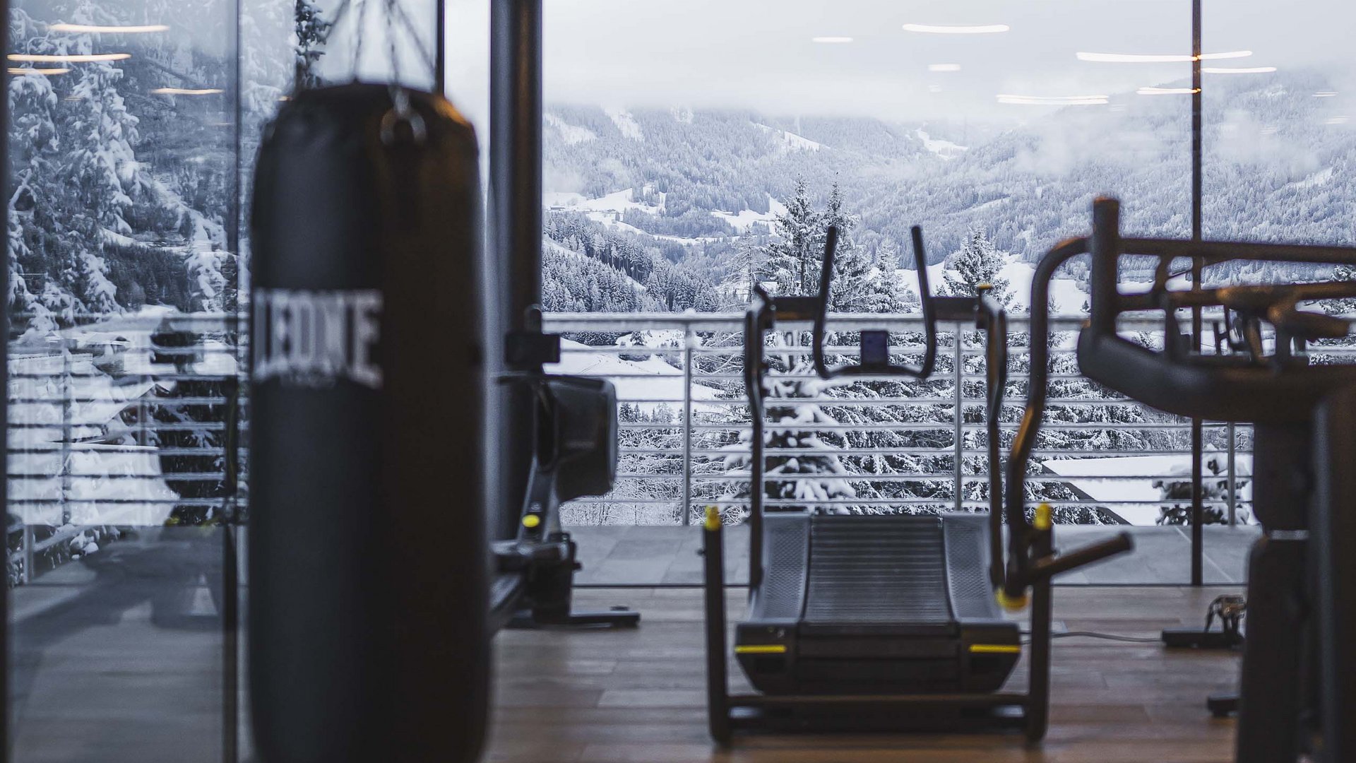 Fitnessraum mit Boxsack und Laufband vor verschneiter Berglandschaft