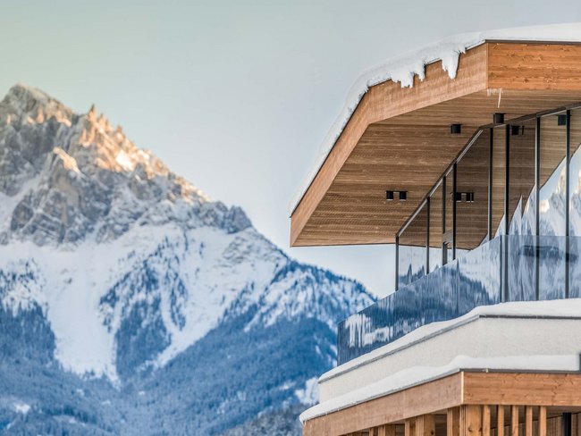 Hotel con vasca idromassaggio in camera in Trentino-Alto Adige Casa moderna con facciata in legno e balcone in vetro davanti a montagna innevata