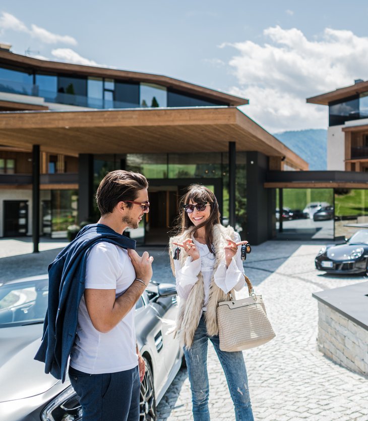 Glückliches Paar mit Autos vor modernem Hotel Alpen Tesitin