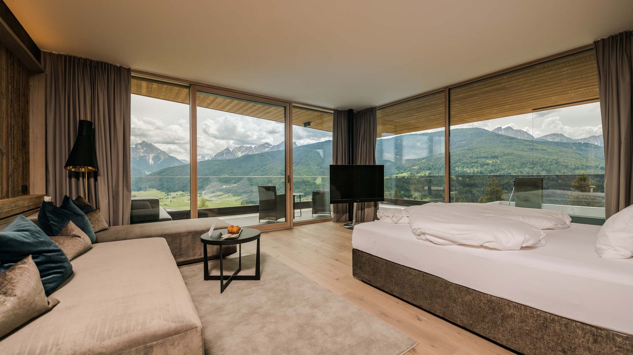Your 5-star hotel in Val Pusteria/Pustertal: Alpen Tesitin Modern hotel room with sofa, bed, and panoramic mountain view