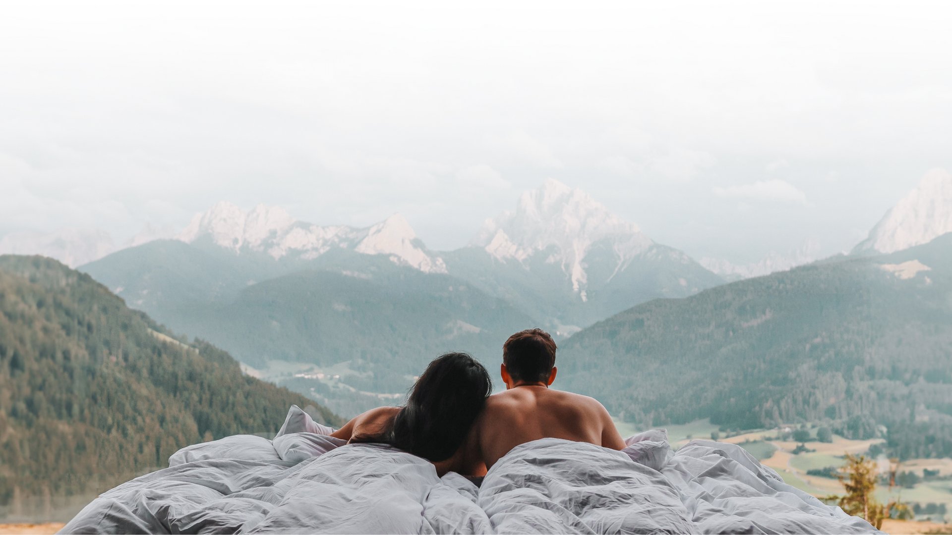 Paar liegt im Bett und blickt auf bewaldete Berge und Gipfel