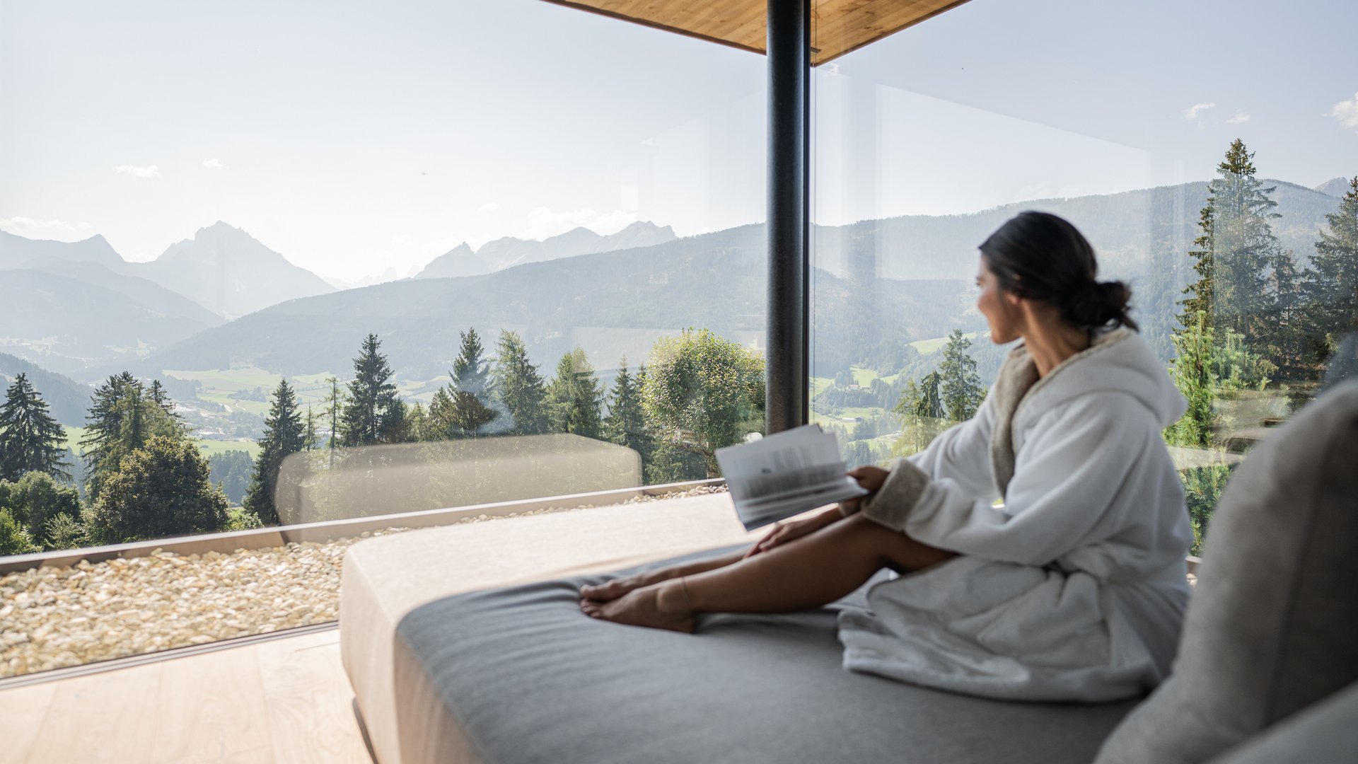 Frau im Bademantel liest auf einem Bett mit Blick auf die Berge