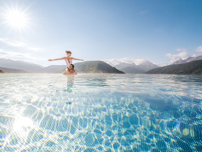 Paar im Pool mit Berg- und Sonnenschein im Hintergrund