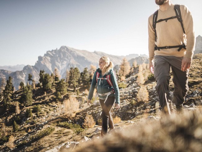 5-Sterne-Sporthotel in Südtirol gesucht? Zwei wandern in den Bergen bei klarem Himmel und herbstlicher Landschaft