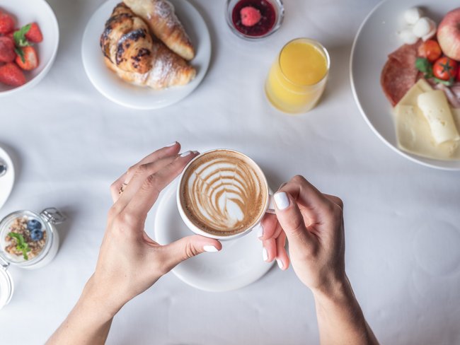 Frühstück mit Cappuccino, Croissants, Saft und Obst auf weißem Tisch