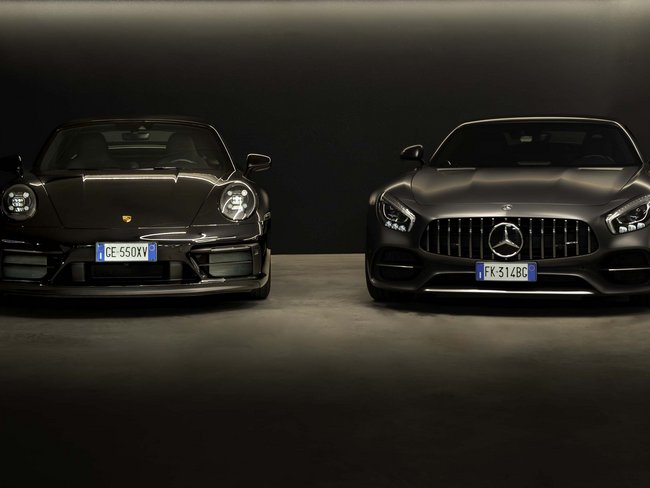 Frontansicht eines schwarzen Porsche und eines schwarzen Mercedes Sportwagens nebeneinander
