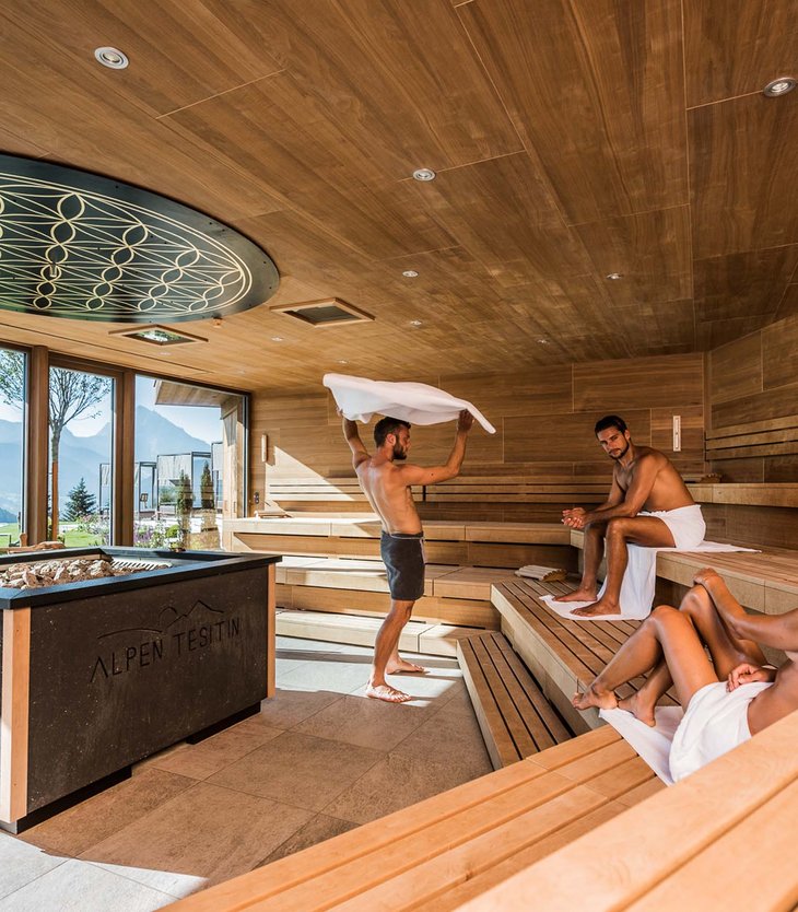 Three people relaxing in a wooden sauna with mountain view and large windows