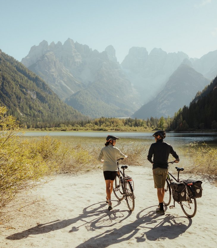 Due ciclisti con caschi vicino a lago di montagna e montagne soleggiate