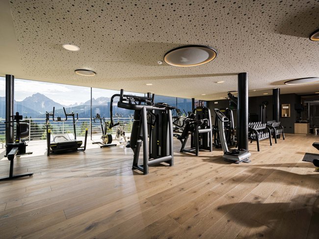 Moderner Fitnessraum mit Geräten und großer Glasfront mit Bergblick