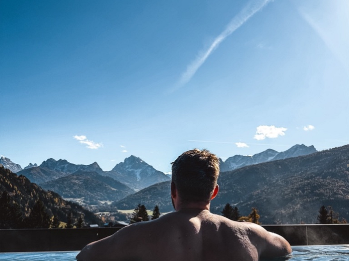 Alpen Tesitin: das sagen unsere Gäste Mann entspannt im Pool mit Blick auf Berglandschaft unter blauem Himmel