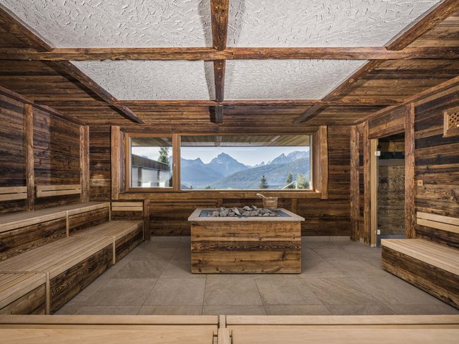 Sala sauna con panche di legno e vista sulle montagne dalla grande finestra