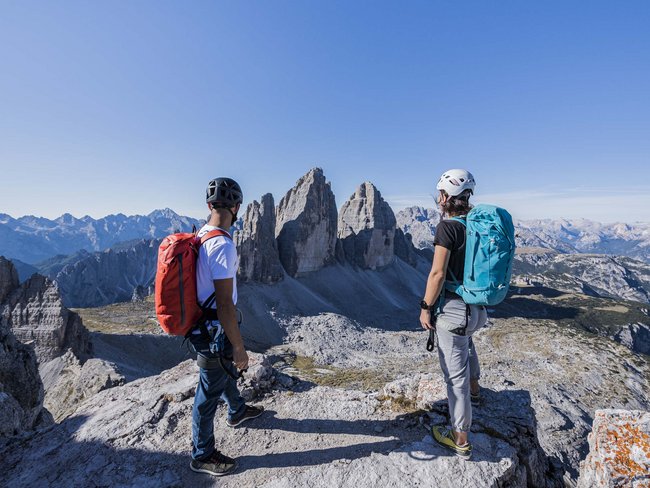 Urlaub im Hotel in den Dolomiten Zwei Wanderer mit Rucksäcken blicken auf die markanten Felsen der Dolomiten