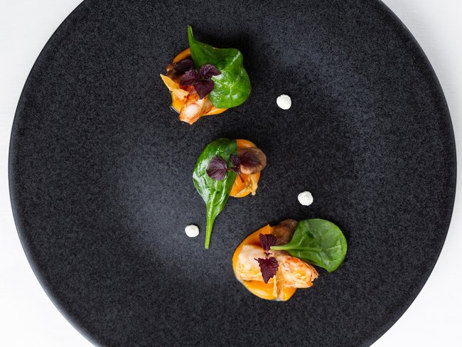 Drei kleine Garnelenhäppchen mit Spinat und Sauce auf schwarzem Teller angerichtet