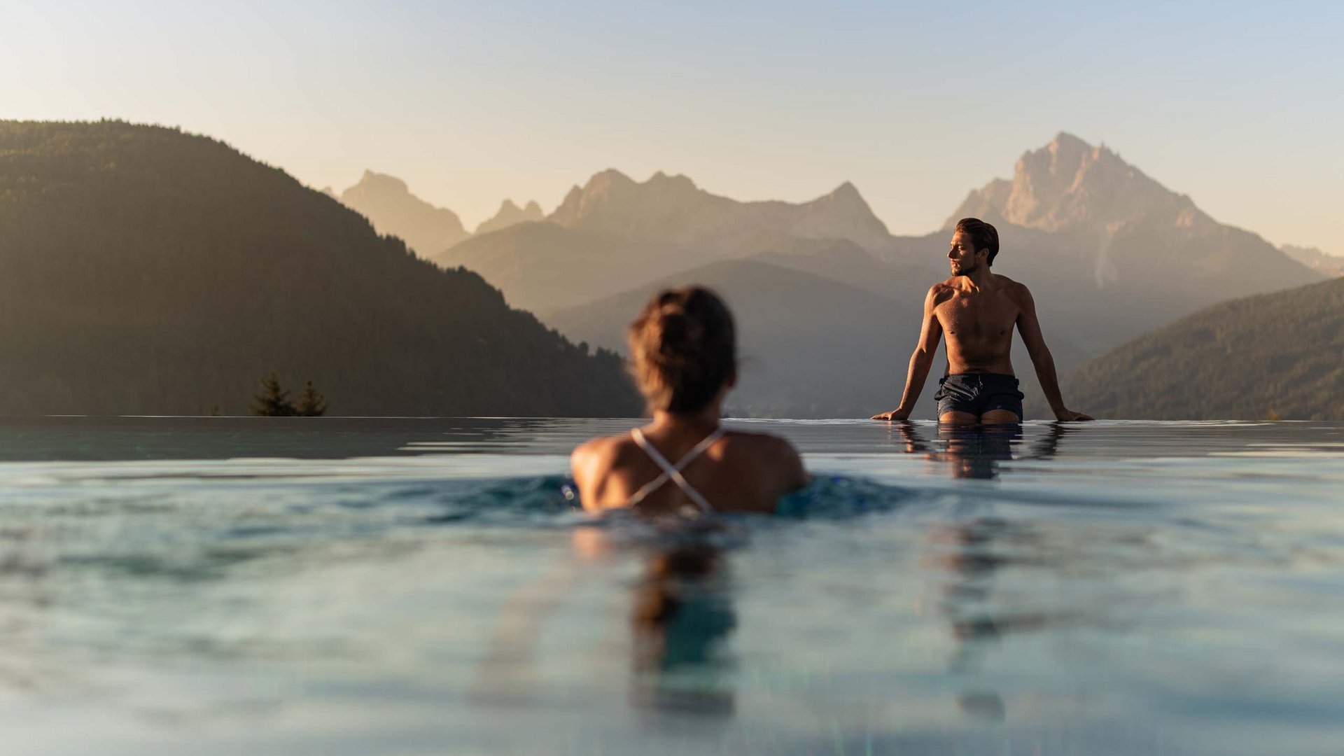 People in infinity pool overlooking mountains at sunset