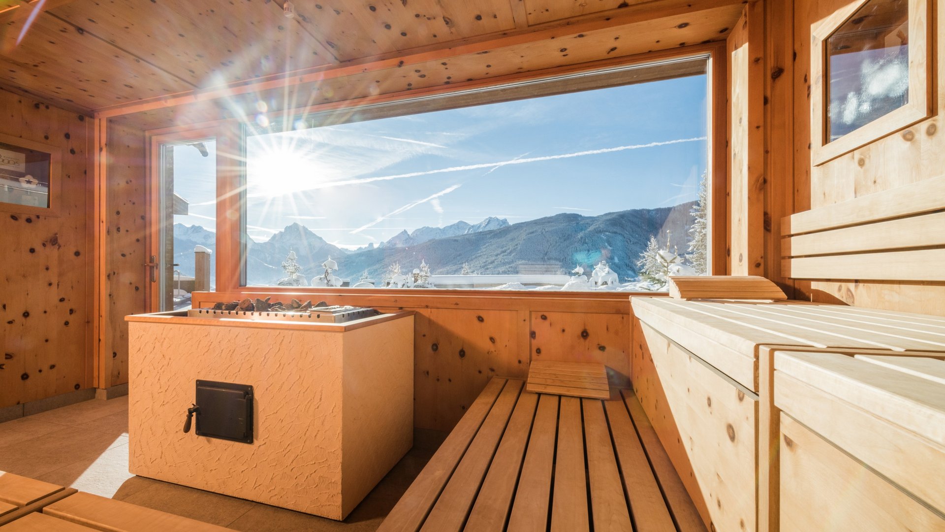 Sauna mit Blick auf schneebedeckte Berge und Sonnenlicht