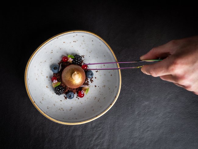 Hand platziert Beere auf kunstvollem Dessert mit Beeren und Creme