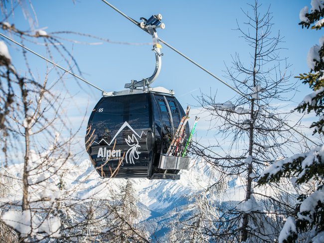 Sciare in Val Pusteria in vacanza all’Alpen Tesitin Cabina funivia nera tra alberi innevati con sci montati all'esterno