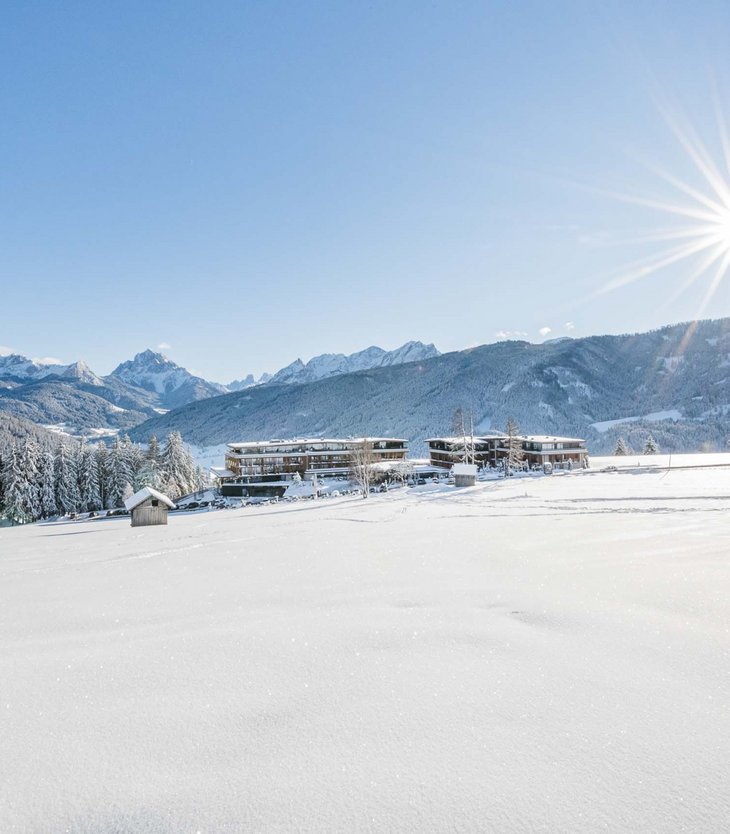 Schneebedeckte Landschaft mit Bergen, Bäumen und Gebäuden unter strahlender Sonne