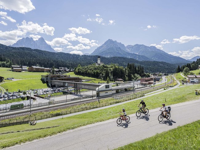 Familie fährt Fahrrad auf Landstraße mit Bergkulisse und Dorf im Hintergrund