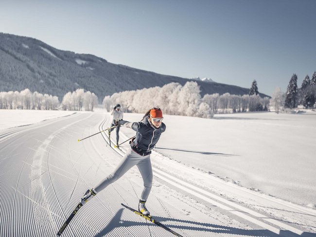 Donna che scia di fondo su paesaggio invernale innevato e soleggiato con montagne