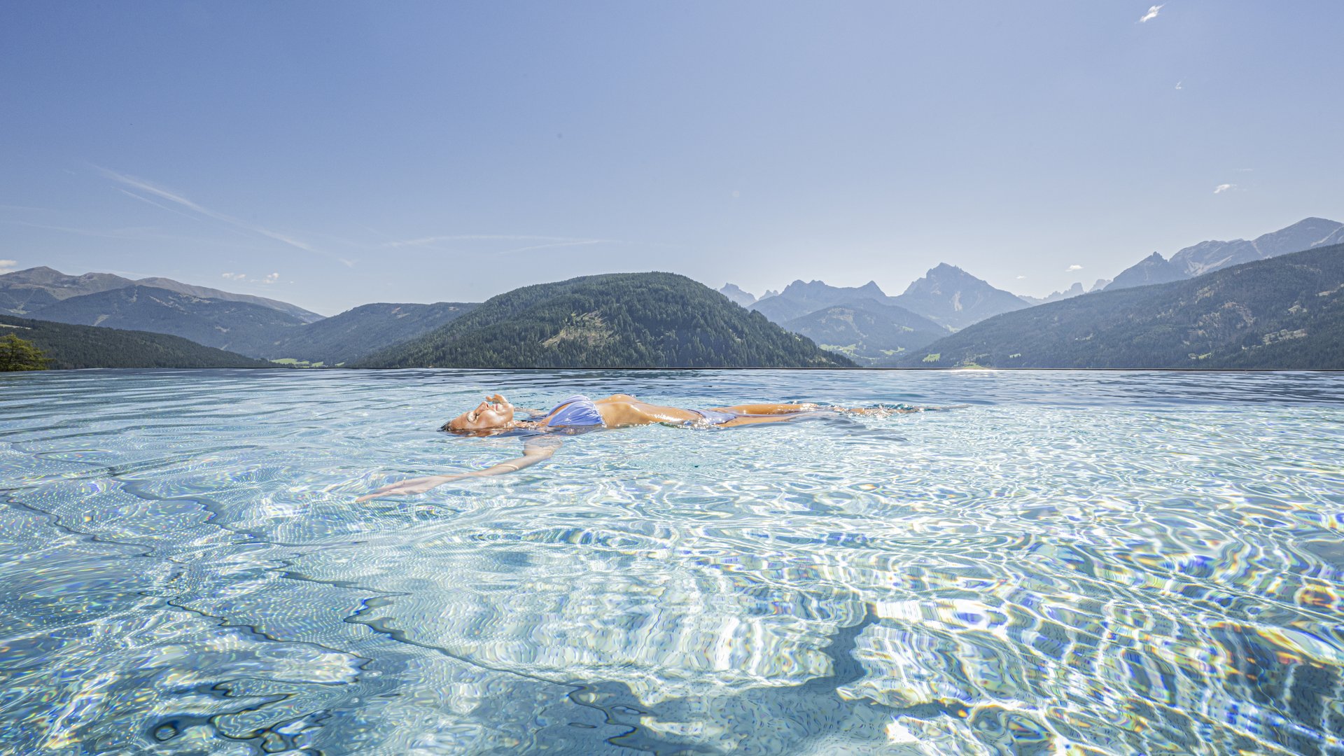 Your hotel in Val Pusteria/Pustertal with pool oasis Person floating in a clear mountain lake with alpine mountains in the background